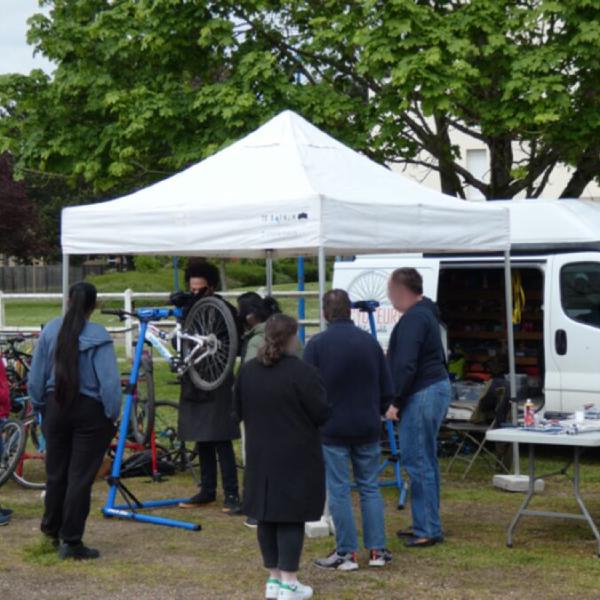 Réparation de vélo en extérieur, le réparateur s'affaire sur le vélo et 6 le regardent.