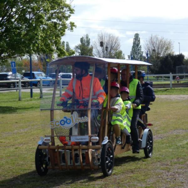 Véhicule à quatre roues en bois avec un animateur et 6 enfants qui pédalent pour le mouvoir